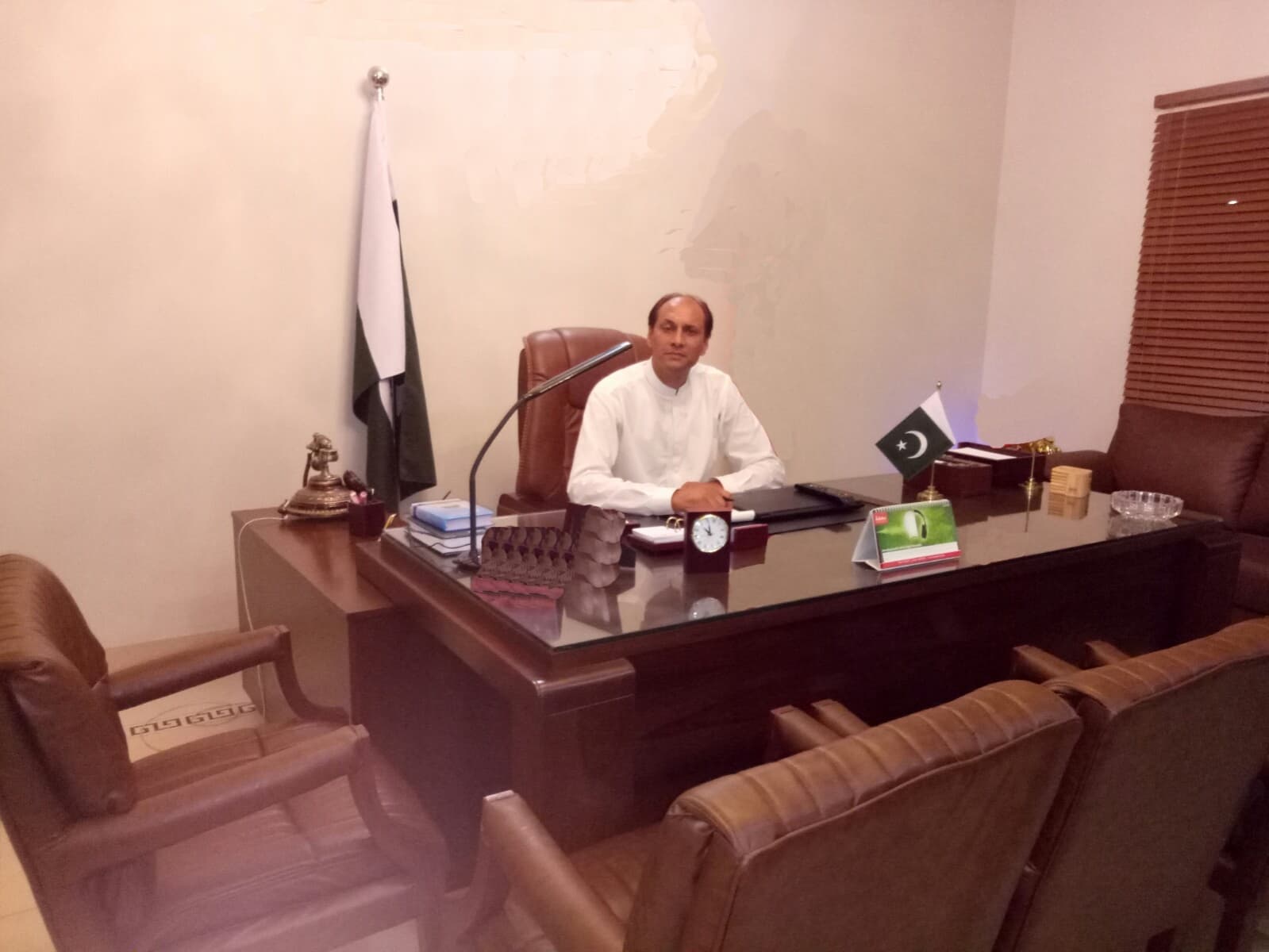 Sardar Altaf Hussain Anwar at secretariat desk with flag and microphone