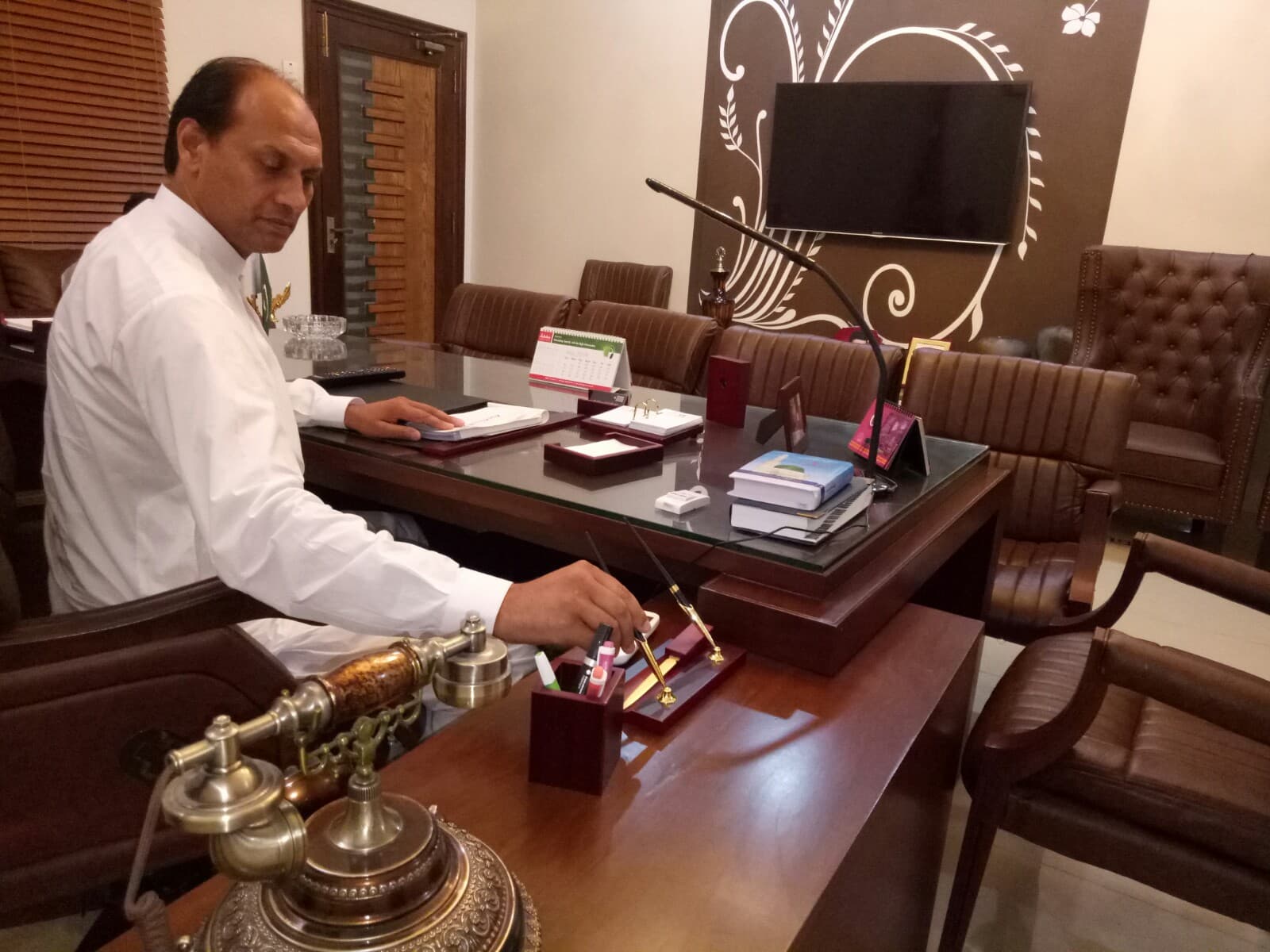 Sardar Altaf Hussain Anwar at desk reaching for pen with published books on table
