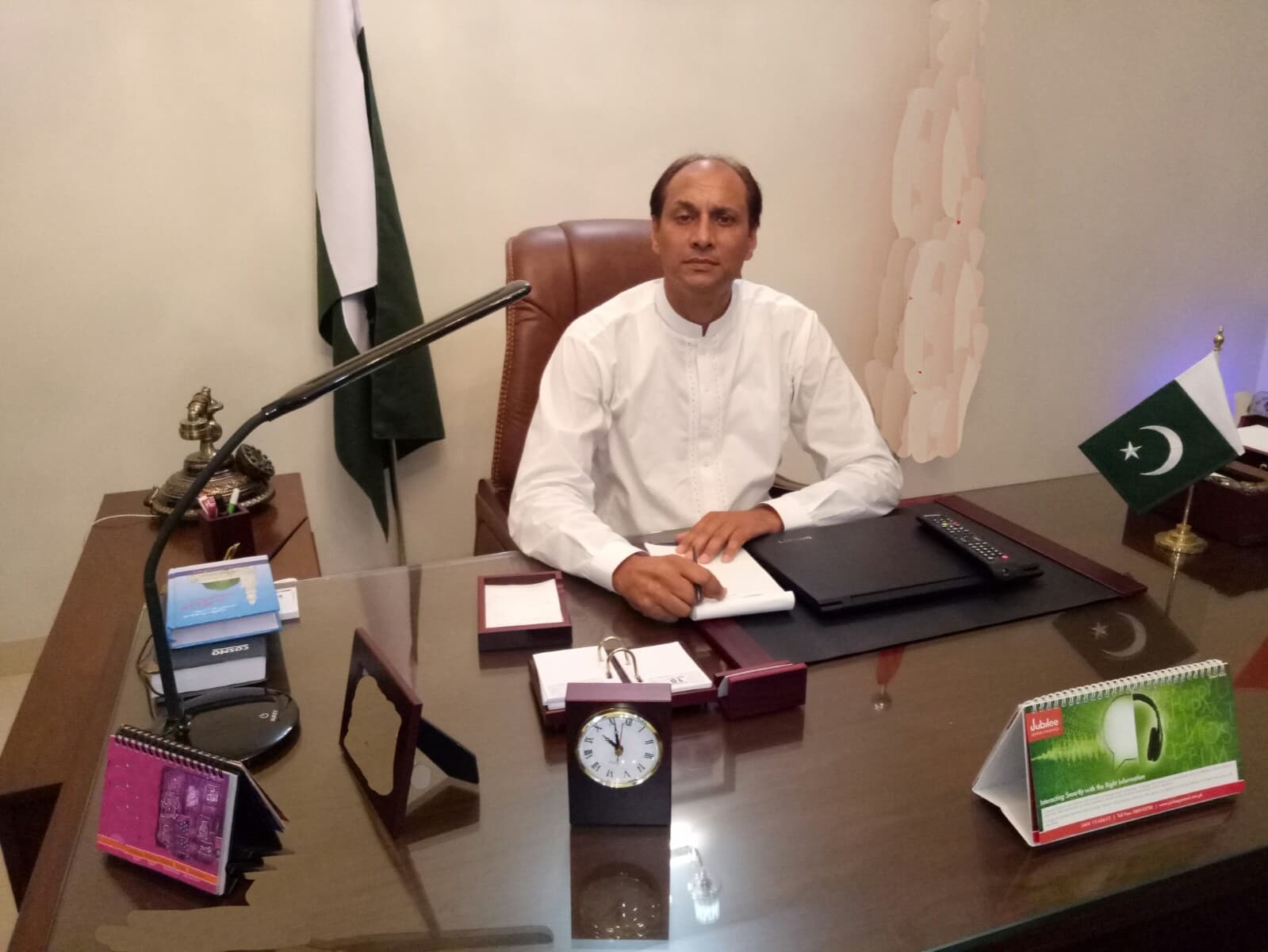 Sardar Altaf Hussain Anwar seated at executive desk with Pakistan national flag behind